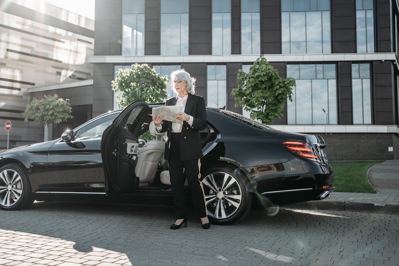 who-we-are Professional adult woman in business attire reading beside a luxury car.